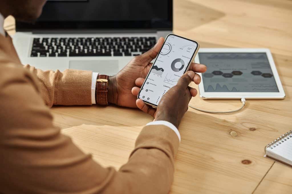 Person using CRM mobile apps on phone with dashboards, near laptop and tablet, showcasing mobile CRM data access.